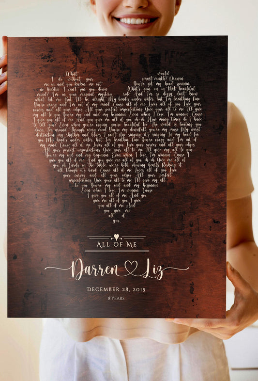 8th Wedding Anniversary song plaque is featured next to a candle. The plaque displays heart shaped lyrics on burnished bronze metal panel. This has full song lyrics arranged in a heart shape in a whimsical calligraphy with the names of the happy couple beneath, and their union date.