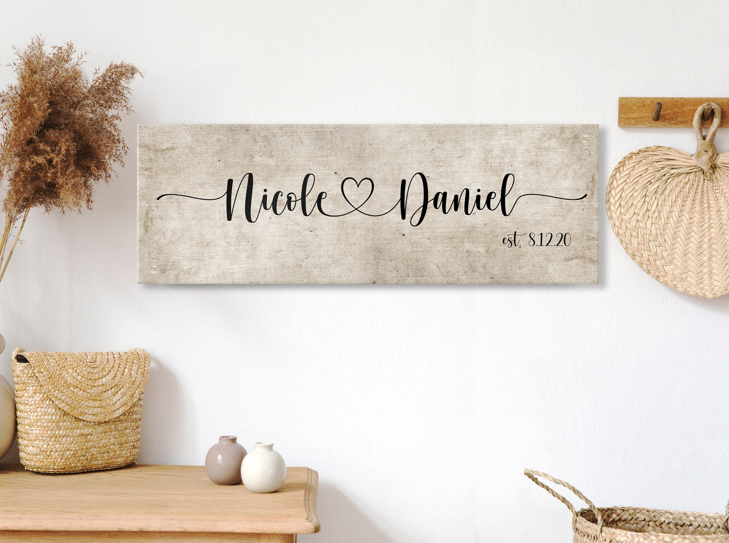 rustic cotton canvas name sign, with 2 first names connected by a heart in a whimsical and playful typeface. A personalized name sign on vintage cotton hangs on wall above bench in entry of home.