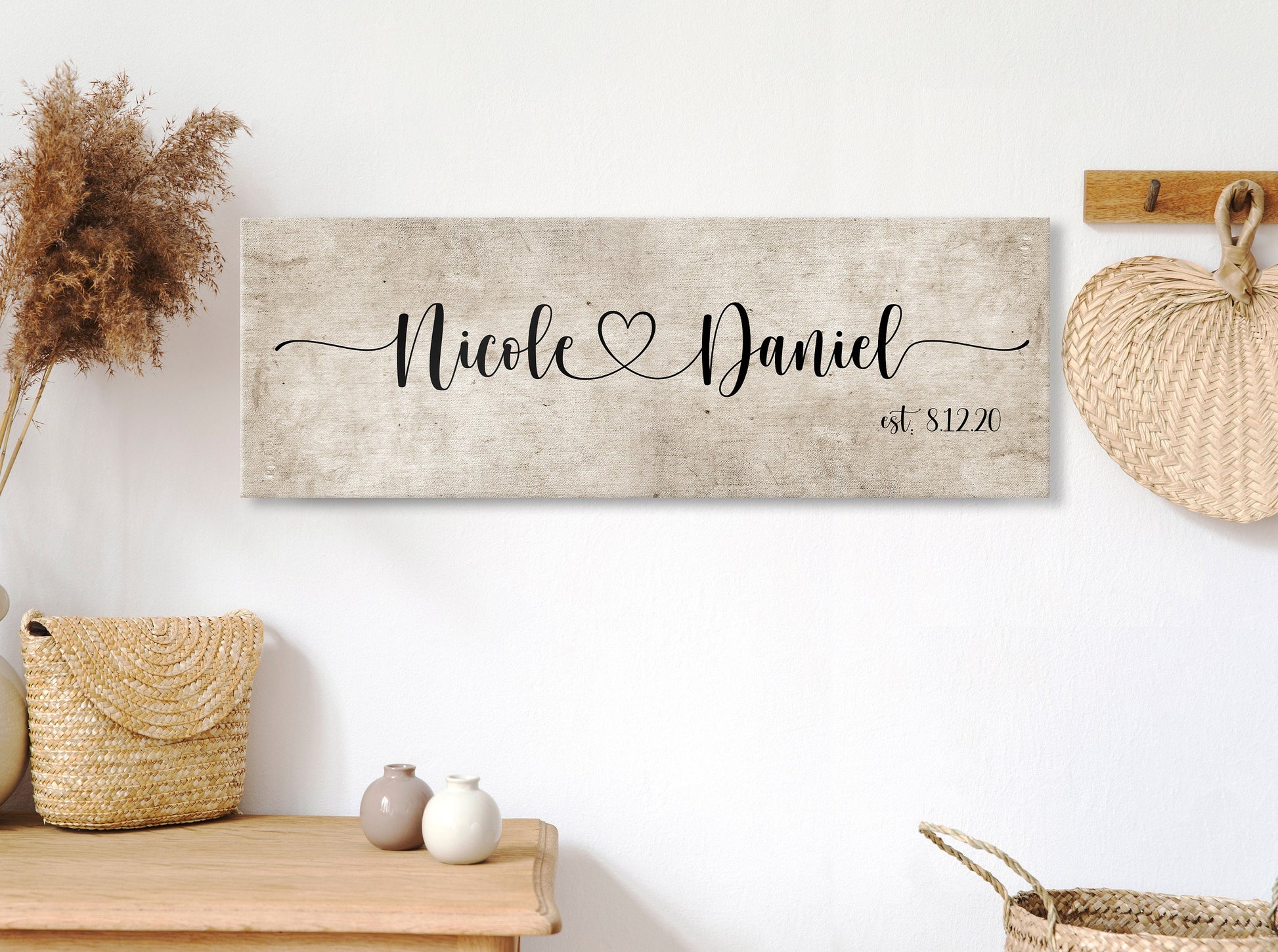 rustic cotton canvas name sign, with 2 first names connected by a heart in a whimsical and playful typeface. A personalized name sign on vintage cotton hangs on wall above bench in entry of home.