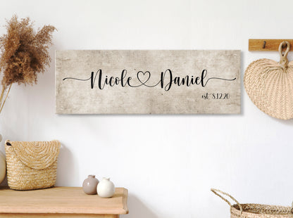 rustic cotton canvas name sign, with 2 first names connected by a heart in a whimsical and playful typeface. A personalized name sign on vintage cotton hangs on wall above bench in entry of home.