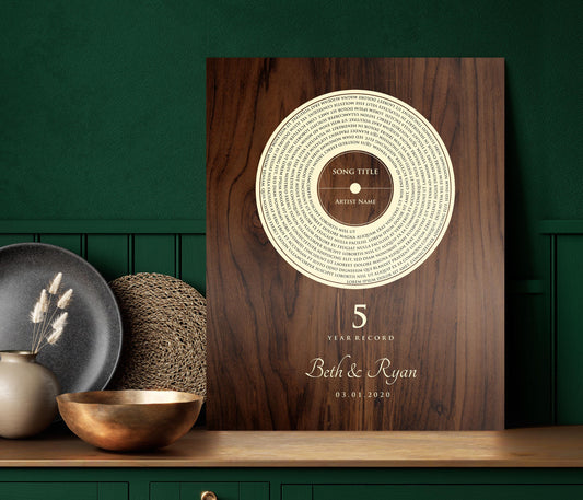 This is a photo of a 5th wedding anniversary, Our 5 Year Record wall plaque is a wood plaque - The record design pops in a natural birch tone set against a deep brown stained and polished birch - featuring song lyrics of choice in a vinyl record motif, accented with the couple's names with a heart symbol between then and the couples wedding date