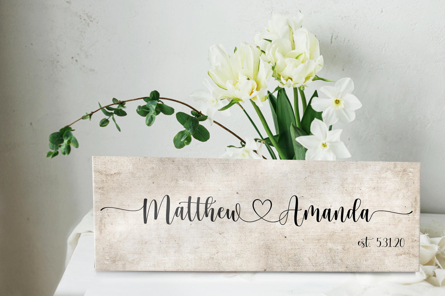 rustic cotton canvas name sign, with 2 first names connected by a heart in a whimsical and playful typeface. A personalized name sign on vintage cotton hangs on wall above bench in entry of home.