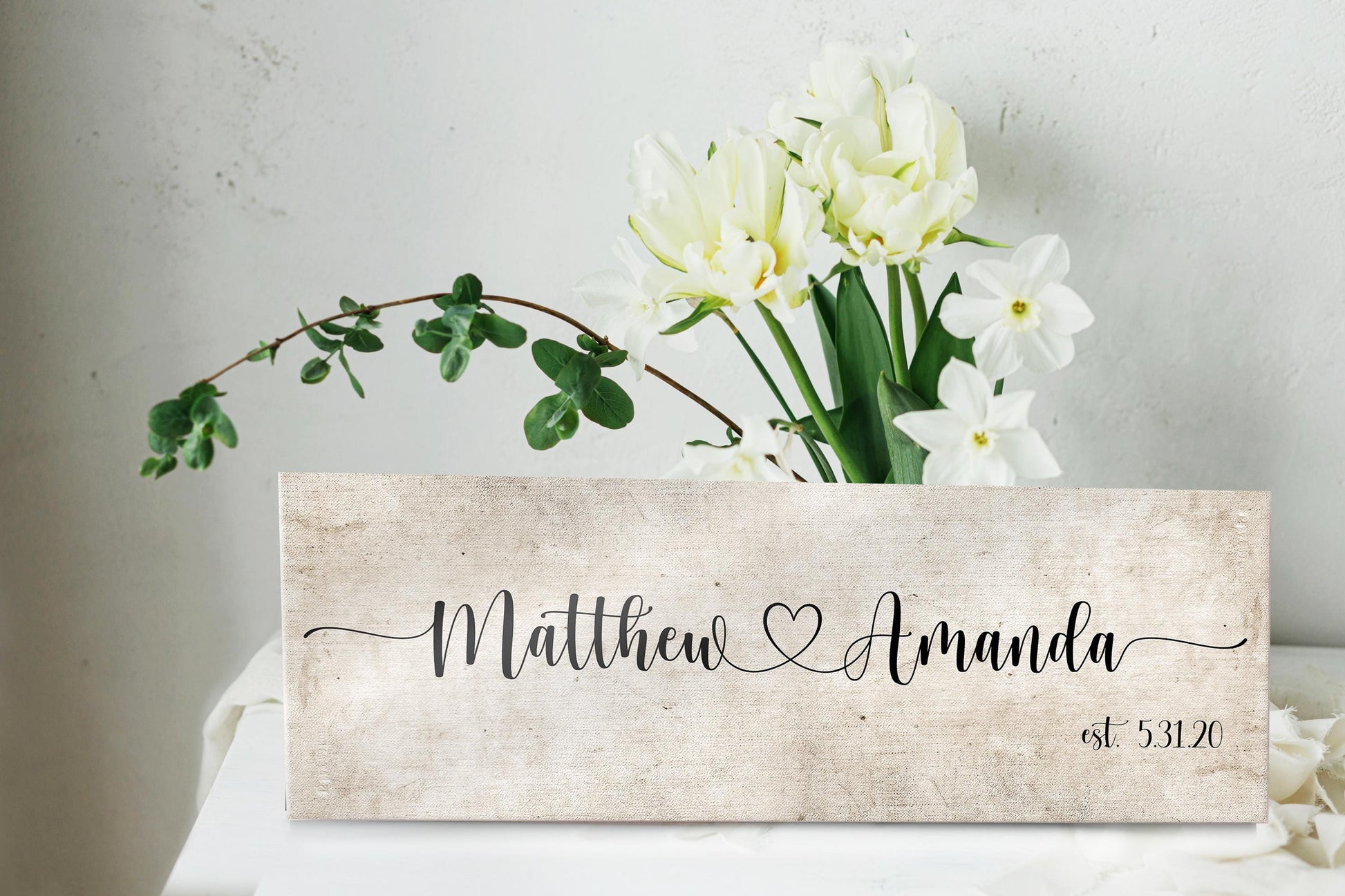 rustic cotton canvas name sign, with 2 first names connected by a heart in a whimsical and playful typeface. A personalized name sign on vintage cotton hangs on wall above bench in entry of home.