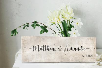 rustic cotton canvas name sign, with 2 first names connected by a heart in a whimsical and playful typeface. A personalized name sign on vintage cotton hangs on wall above bench in entry of home.