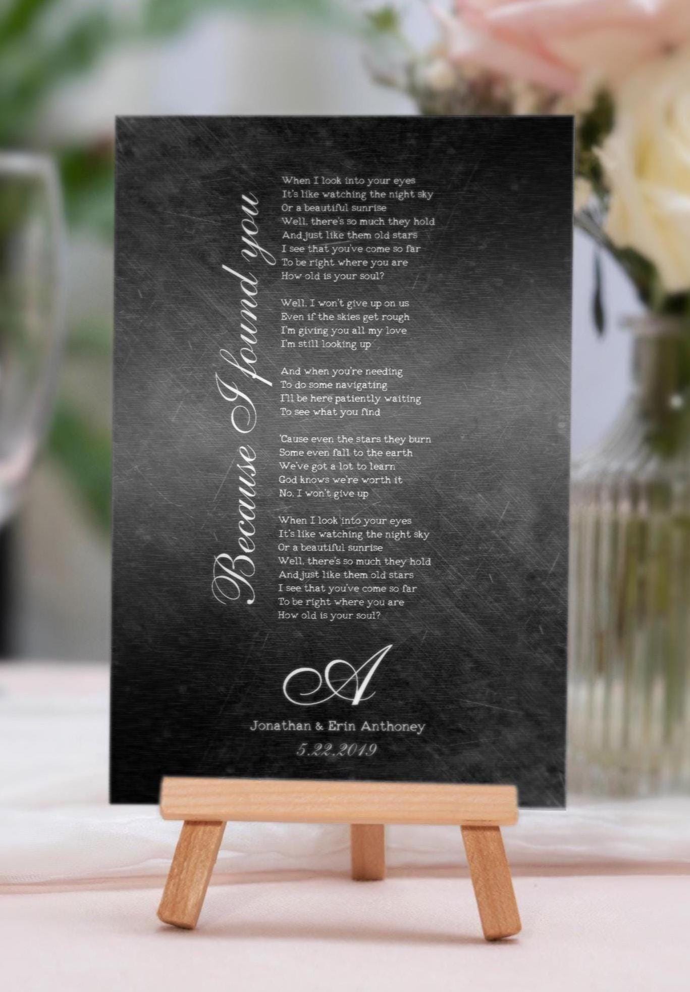 Song lyric art for the iron anniversary or 6 year anniversary gifts: A Distressed and dark metal, iron-alloy plaque sits on a tabletop easel, with a song inscribed in vintage type font, and the song title running along the left side of the wording from bottom to top in a beautiful calligraphy. It's finished with an elegant monogram letter, a couple's names and union date for a romantic and sentimental tribute to their first dance.