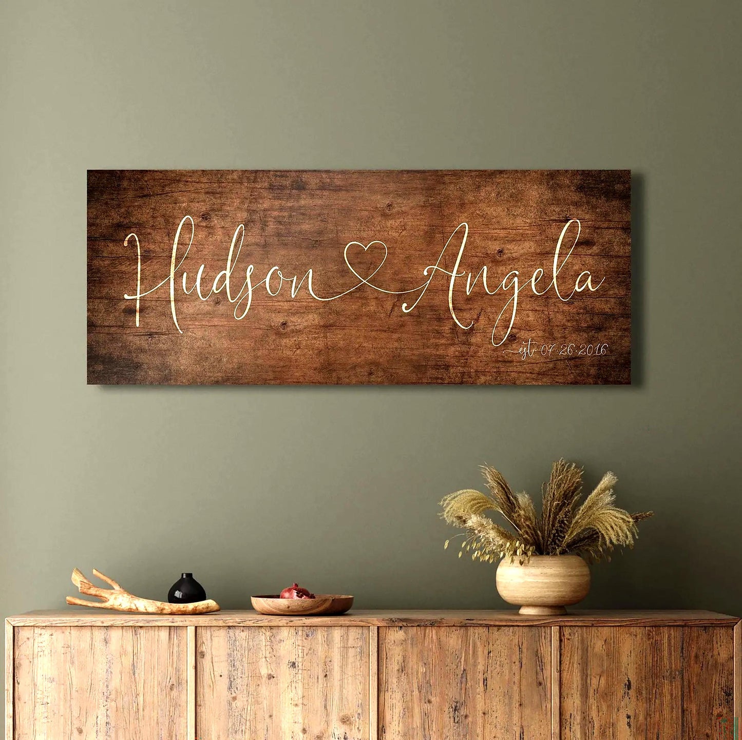 One Heart Between Us: Couples Rustic Name Sign
A rustic wood sign featuring the names of a couple in whimsical calligraphy, connected by a single heart, hangs above a sideboard in a distressed aged birch finish. 
Courtesy of Honeycomb Proverbs