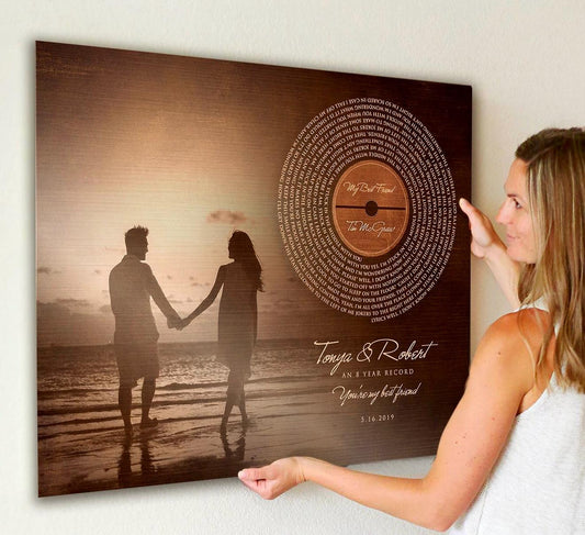 An attractive woman is hanging a bronze anniversary plaque on her wall. This anniversary Photo Gift and burnished bronze keepsake blends a favorite photo with a vinyl record-inspired motif, displaying the full song lyrics in a striking spiral. Below the record, an excerpt from the lyrics, years married, couples names, and est. date complete this timeless piece.