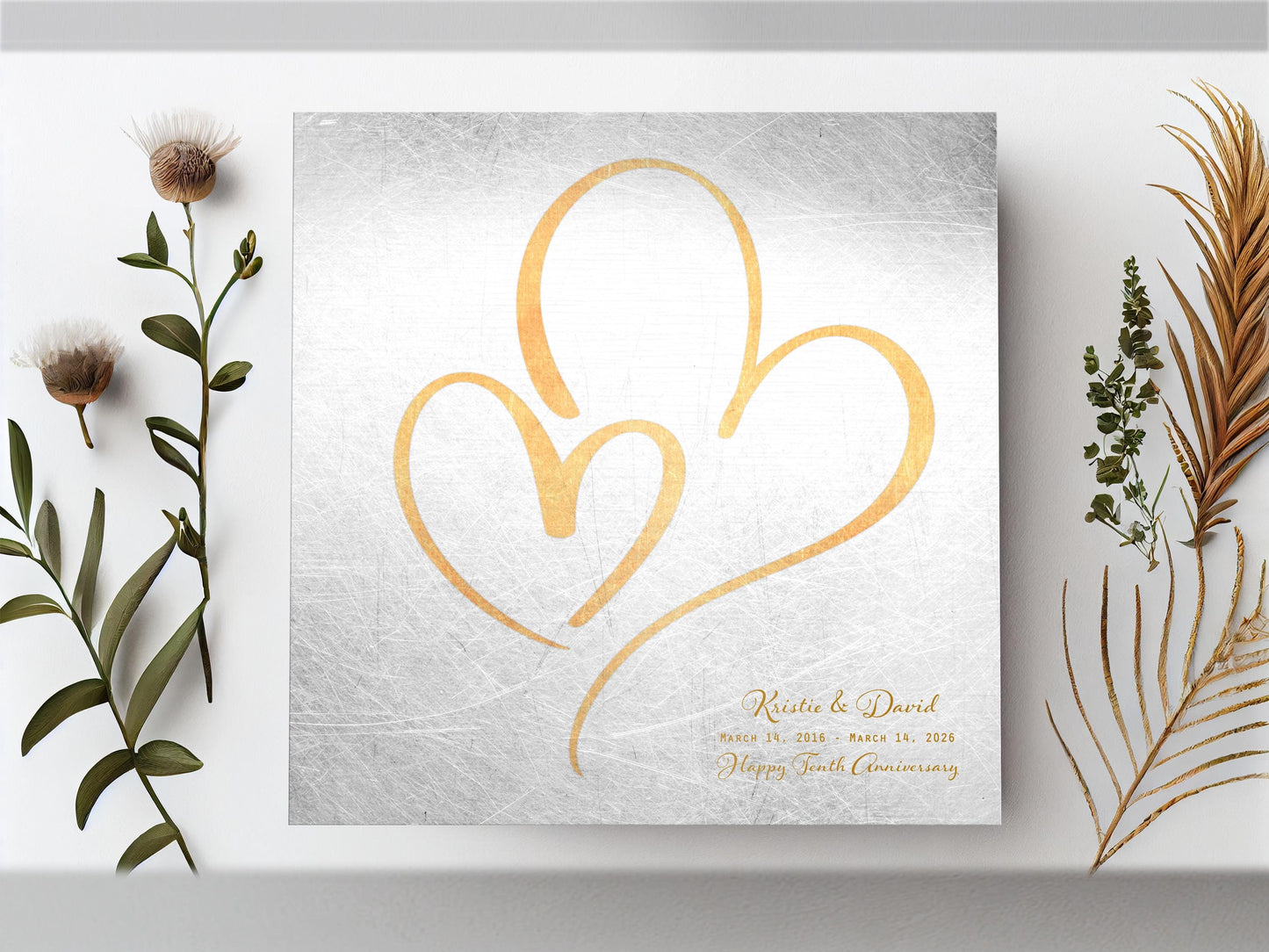 Couples Tin Hearts Distressed Anniversary wall plaque features an elegant brass-toned larger heart enveloping a delicate smaller brass-toned heart. Plaque includes personalization of first names, and a Happy Tenth Anniversary Wish on the bottom right. Wedding date to Anniversary date is highlighted beneath the couples names.