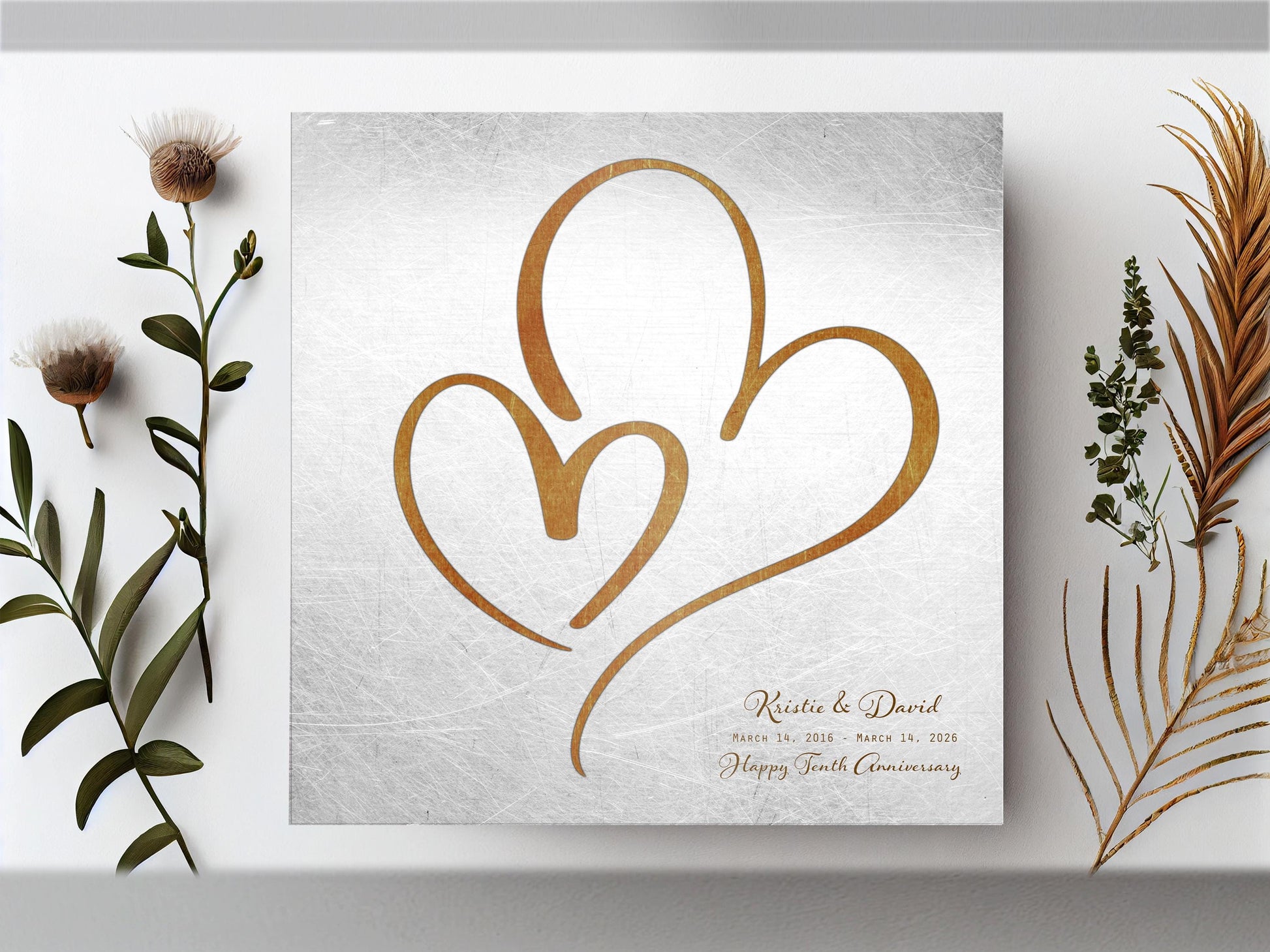 Couples Tin Hearts Distressed Anniversary wall plaque features an elegant bronze-toned larger heart enveloping a delicate smaller bronze-toned heart. Plaque includes personalization of first names, and a Happy Tenth Anniversary Wish on the bottom right. Wedding date to Anniversary date is highlighted beneath the couples names.