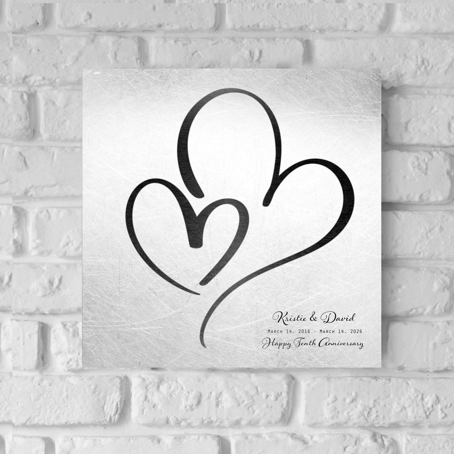 Couples Tin Hearts Distressed Anniversary wall plaque features an elegant black-toned larger heart enveloping a delicate smaller black-toned heart. Plaque includes personalization of first names, and a Happy Tenth Anniversary Wish on the bottom right. Wedding date to Anniversary date is highlighted beneath the couples names.