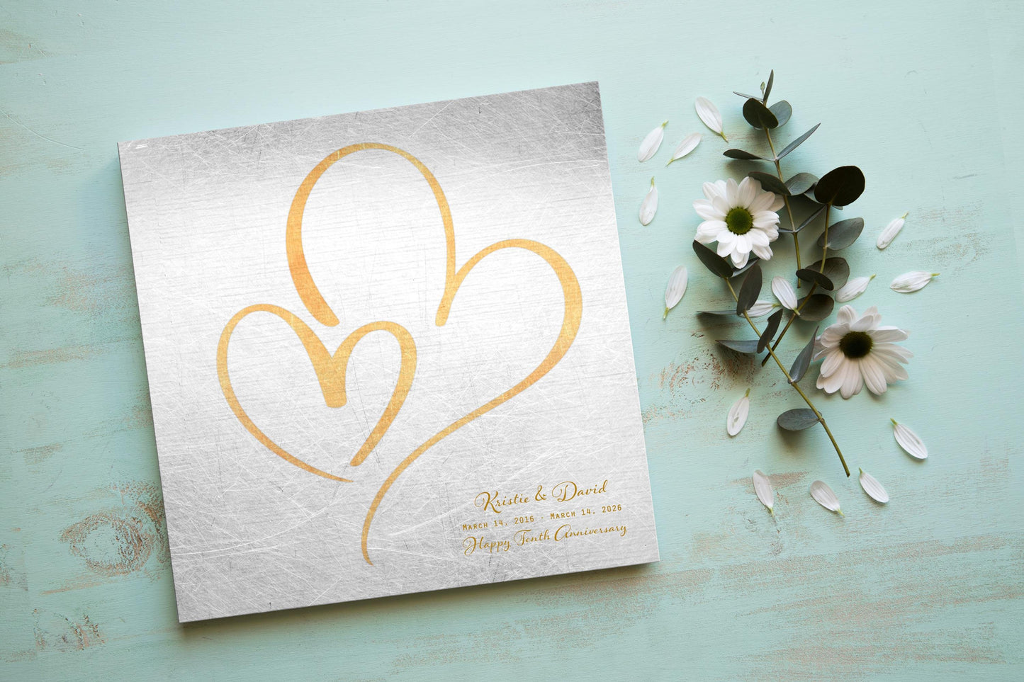 Couples Tin Hearts Distressed Anniversary wall plaque features an elegant brass-toned larger heart enveloping a delicate smaller brass-toned heart. Plaque includes personalization of first names, and a Happy Tenth Anniversary Wish on the bottom right. Wedding date to Anniversary date is highlighted beneath the couples names.
