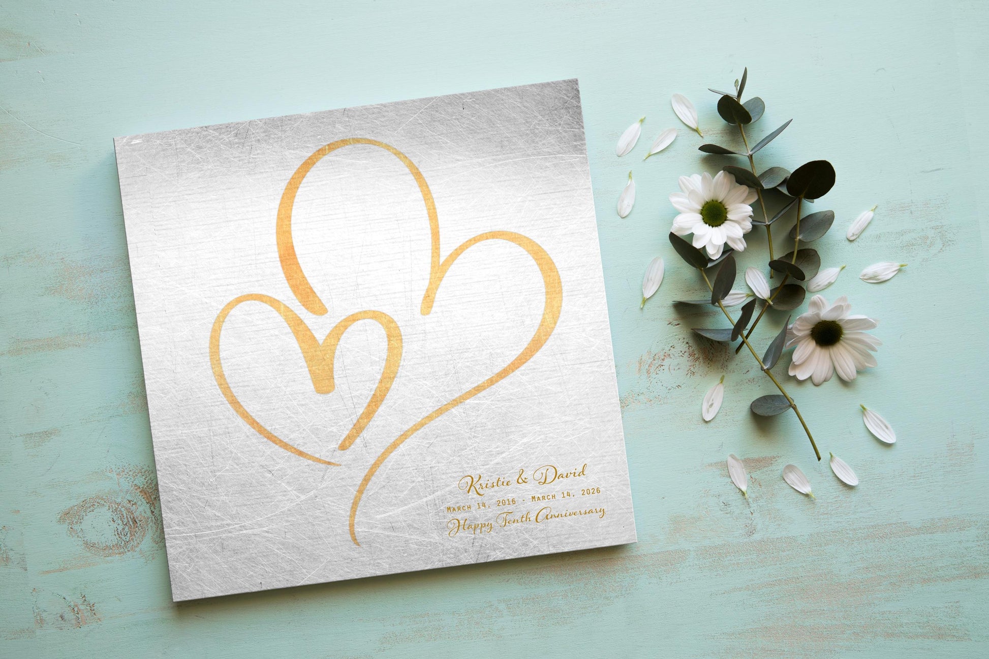 Couples Tin Hearts Distressed Anniversary wall plaque features an elegant brass-toned larger heart enveloping a delicate smaller brass-toned heart. Plaque includes personalization of first names, and a Happy Tenth Anniversary Wish on the bottom right. Wedding date to Anniversary date is highlighted beneath the couples names.
