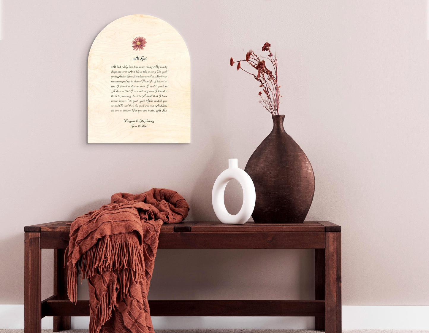 Custom lyrics song plaque in an arch shaped on natural pine, features a blush colored daisy flower motif seated above the song title "At Last" with the lyrics beneath. The plaque is finished with the names and wedding date of the recipient of this couple's plaque. The inscription is an elegant yet easily readable calligraphy script in deep coffee.