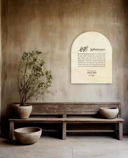 An arch shaped natural wood wall plaque personalized with a family last name Johanson, and the bible verse, Joshua 24.15 in a modern typeface. Under the verse, sits an address, and the family's established date, with a decorative motif accent beneath.