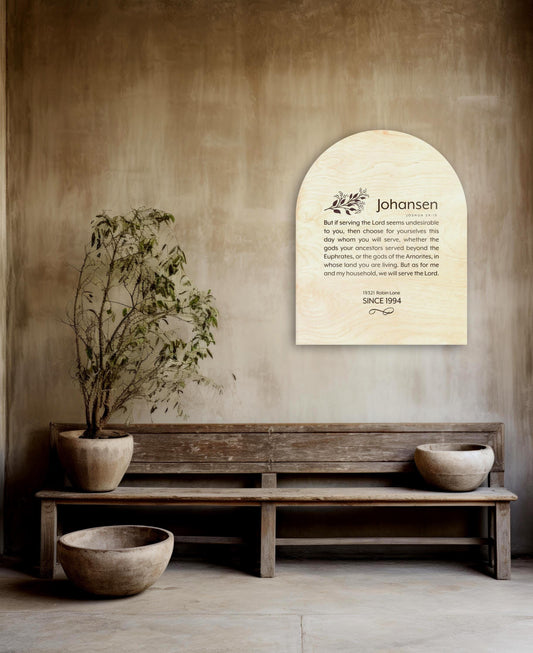 An arch shaped natural wood wall plaque personalized with a family last name Johanson, and the bible verse, Joshua 24.15 in a modern typeface. Under the verse, sits an address, and the family's established date, with a decorative motif accent beneath.
