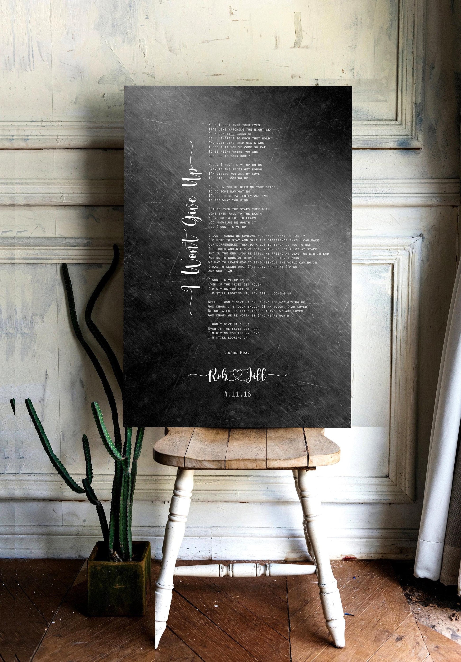 A distressed metal song plaque personalized with the names "Rob & Jill" and the date "4.11.16", sits on a chair.