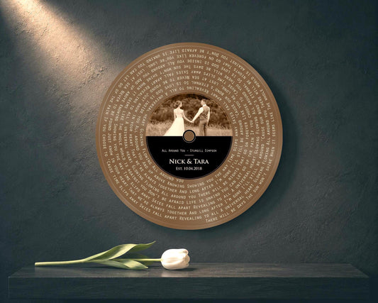Bronze round song lyrics record with sepia couple photo and Nick and Tara label on a dark teal wall, white tulip on the shelf
