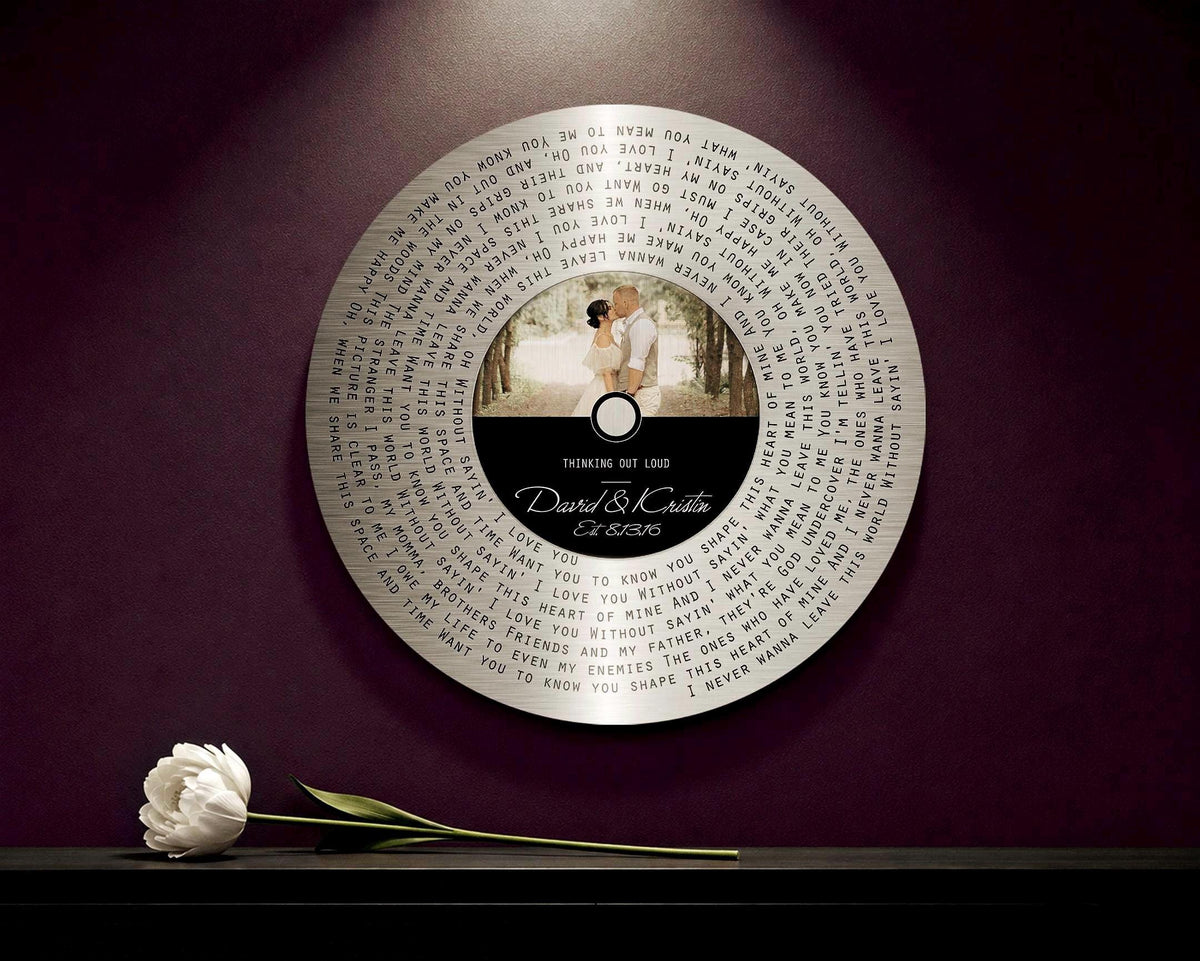 Round tin song lyrics record with couple photo and first dance lyrics, shown on a burgundy wall
